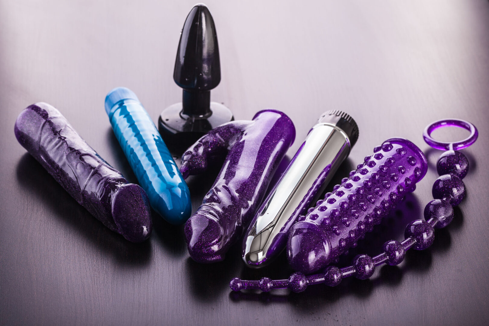 a collection of different types of sextoys, including dildo, vibrators and butt plugs over a dark wooden surface